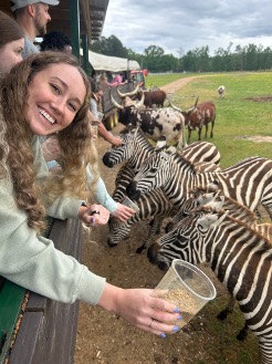 a resident smiles while feeding a zebra from a petting zoo train